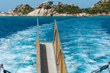 A shot of the wake left by the yacht on the blue sea with in the background the cliff and the Mediterranean scrub by day with the sun on summer, in Sardinia Italy