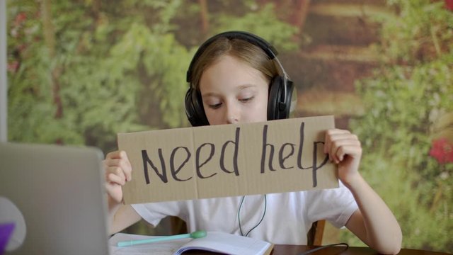 Sad teenager girl in headphones holding in hands cardboard tablet with inscription need help. Unhappy girl in music earphones showing lettering need help