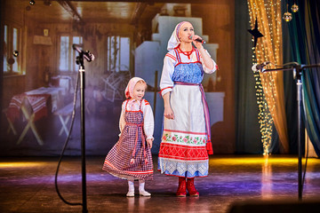 A little girl and an adult woman in Russian national dress rehearsing on stage. Mother and daughter sing and dance together