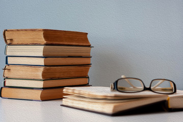 A simple composition of several old books on a white modern table with light gray background, back to school, education. One book is opened with glasses on top