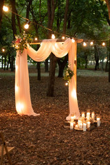 Wedding arch in the woods with light bulbs. Beautiful wedding rustic in the forest. Seats for guests at a beautiful wedding with light bulbs in the forest. Overall plan.