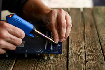 Technician or engineer is focused on repairing circuit board with soldering iron.