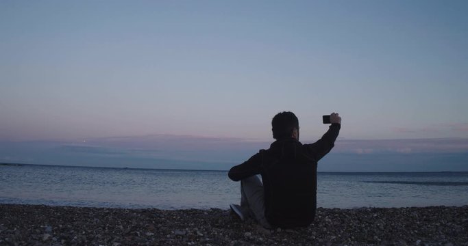 Boy on the beach during a sunset taking a selfie
