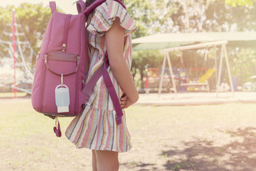 student girl carrying schoolbag with hand sanitizer clip on near playground, school reopening, return back to school after covid-19 coronavirus pandemic is over, new normal concept