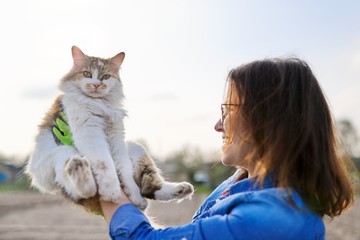 Outdoor woman holding domestic cat in arms and talking to her