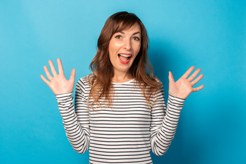 Portrait of a young friendly woman with a surprised face in a casual t-shirt on an isolated blue background. Emotional face. Gesture of surprise, delight, shock