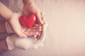 Doctor hands with medical gloves holding child hands and red heart, health insurance, donation,...