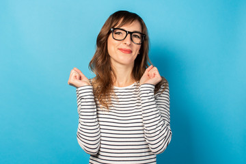 Portrait of a young friendly woman in casual t-shirt and glasses very emotionally happy about something on an isolated blue background. Emotional face. Gesture of celebration