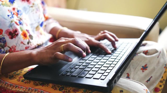 Closeup of the hands of a woman wearing golden bangles and ring using a laptop