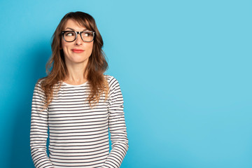 Cute Young woman smiling with glasses and a striped sweater looks away on an isolated blue background. Emotional face. Concept surprise, pay your attention