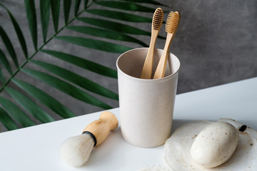 Set of eco-friendly bathroom accessories on table. Natural wooden toothbrushes in glass, shaving brush, organic soap. Zero waste, plastic free, sustainable lifestyle concept