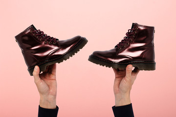 Hands hold boots on a pink background. The concept of choosing shoes, shopping, shoe repair. Concept of shoe selection, shopping, shoe repair