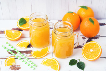 Orange juice in glass jars and fresh oranges on a white wooden rustic background.