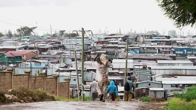 People walking on murram road heading to a slum