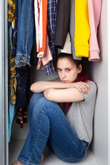 Young girl sad sits in wardrobe. House violence, coming out