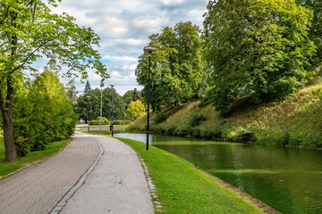 Fototapeta na wymiar A pond in Snelli park, Tallinn, Estonia. Green trees and sidewalk on summer day with clouds.