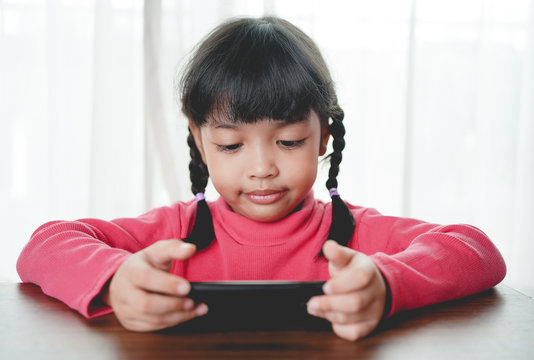 Cute asian child girl playing a smart phone, Smart phone has a negative impact on your child’s development and mental health. but if using in a good way, it will improve unlimited skill to a child.