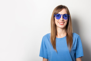 Portrait of a young friendly woman in casual blue t-shirt and blue glasses smiling on an isolated light background. Emotional face