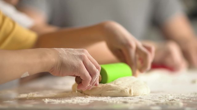 Children cooks pizza. Boy and girl having fun with father. Prepering ingredients for pizza. Roll out the dough with a rolling pin