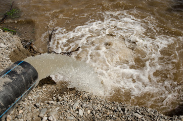 a strong stream of water pouring from a plastic water pipe into a river