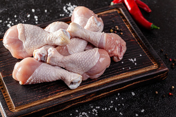 Raw meat. Chicken legs lie on a wooden board with vegetables and spices on a black background. background image, copy space text