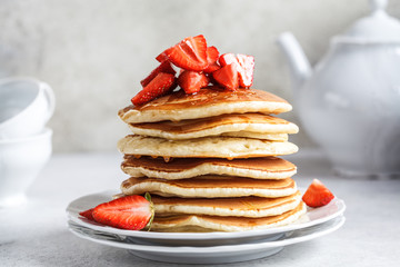 Pancakes with strawberries and honey on white plate.
