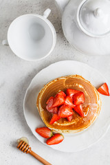 Pancakes with strawberries and honey on white plate, top view.