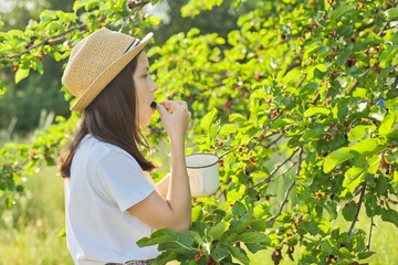 Girl with pleasure eating delicious sweet ripe berries from mulberry tree