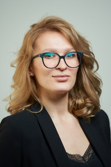 Fototapeta premium A stylish young woman in glasses dressed in a black suit with a black shirt. A close-up portrait of a blond lady who wears a business outfit. A concept of an office style wardrobe.