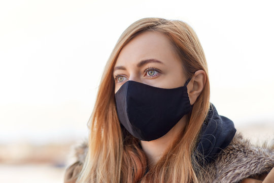 health, safety and pandemic concept - young woman wearing black face protective reusable barrier mask outdoors