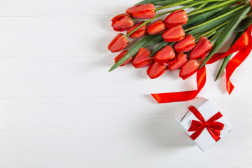 Red tulips and a gift on a white table. Mother's Day, copy space.