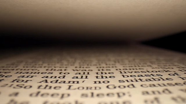 Zoomed into "God made a woman" and then moving up the first page of the Bible, passing by Genesis 2:18 "It is not good for man to be alone"; rising above slightly as shot ends.