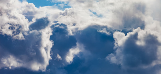 Dark blue Cumulus clouds against a blue sky, illuminated by the sun