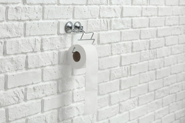 Holder with roll of toilet paper hanging on wall
