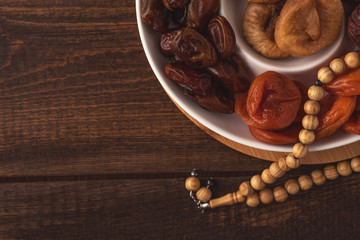 iftar concept, plate of dried fruit and prayer beads on brown wooden table, Ramadan month