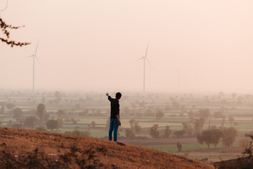Indian man standing on top of hill in front of the windmills during the sunset at Wankaner, Gujarat, India