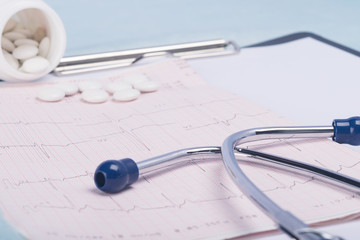 on a light background, cardiogram of a heartbeat, phonoscope, drugs for treatment and a notebook for recording the results of a patient examination, close-up