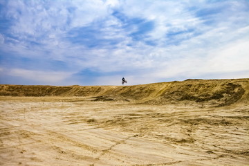 Motorcyclist on a sand quarry against the sky with clouds in the summer