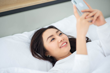 Obraz na płótnie Canvas Asian woman type and chat on mobile phone in the bed