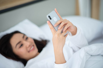 Asian woman type and chat  on mobile phone in the bed