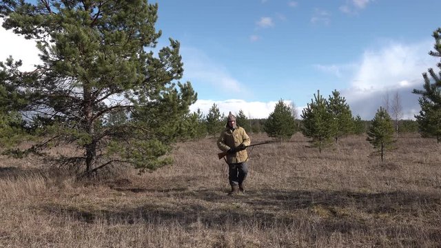Man hunter soldier Red Army going the forest field and shoots firing a shotgun