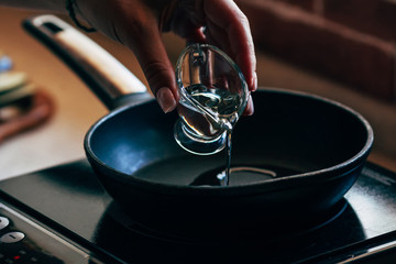 A female hand pours olive oil into a pan.