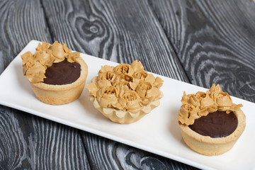 Chocolate ganache tartlets and cakes. Decorated with oil cream flowers. The cream has a caramel color. On brushed pine boards painted black.