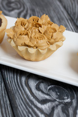 Half a cake decorated with butter cream flowers. The cream has a caramel color. On brushed pine boards painted black.