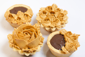 Chocolate ganache tartlets and cakes. Decorated with oil cream flowers. The cream has a caramel color. On white background.