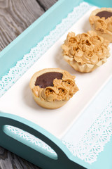 Chocolate ganache tartlets and cakes. Decorated with oil cream flowers. The cream has a caramel color. In a tray of turquoise color.