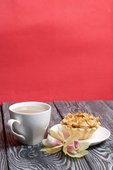 Cupcake and a cup of coffee with milk. Nearby are orchid flowers. Cake decorated with flowers made of butter cream. The cream has a caramel color. On brushed pine boards painted black.