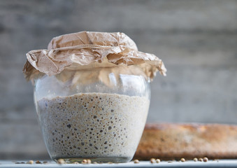 sourdough on whole grain flour in glass jar and loaf rye bread on table, yeast-free leaven starter...