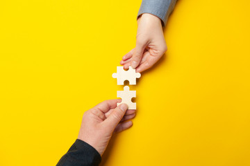 Fototapeta na wymiar Two hands connect puzzles on a yellow background. Cooperation and teamwork in business. Collaboration people for success.