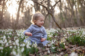 Little pretty girl in a clearing of snowdrops. A child walks in the spring forest.